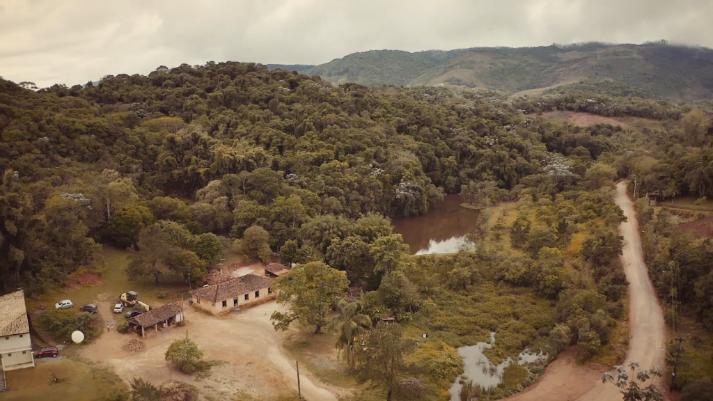 Cena do filme “Serráqueos”: A Serra de Itapeti vista do alto. Entre a vegetação, uma clareira abriga a sede a unidade de conservação